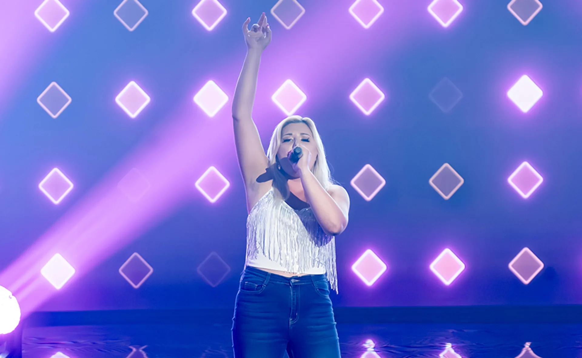 Steffii puts her arm in the air while singing on The Voice stage