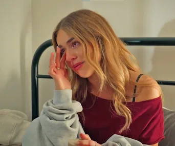 Ally sits on a bed, looking tearful