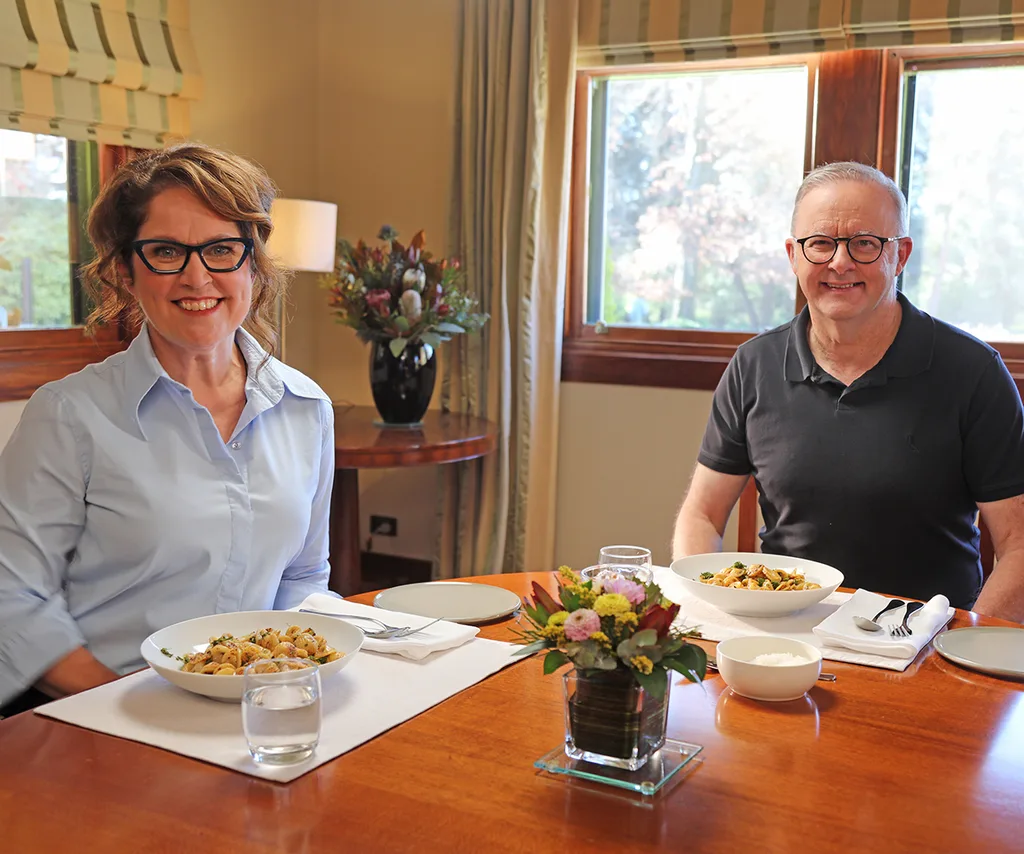 Annabel is sitting next to Anthony Albanese in a kitchen with food on the table in front of them