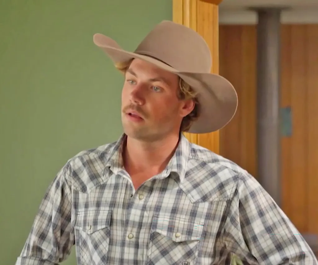 Dylan, wearing a cowboy hat and a checked shirt, inside his house