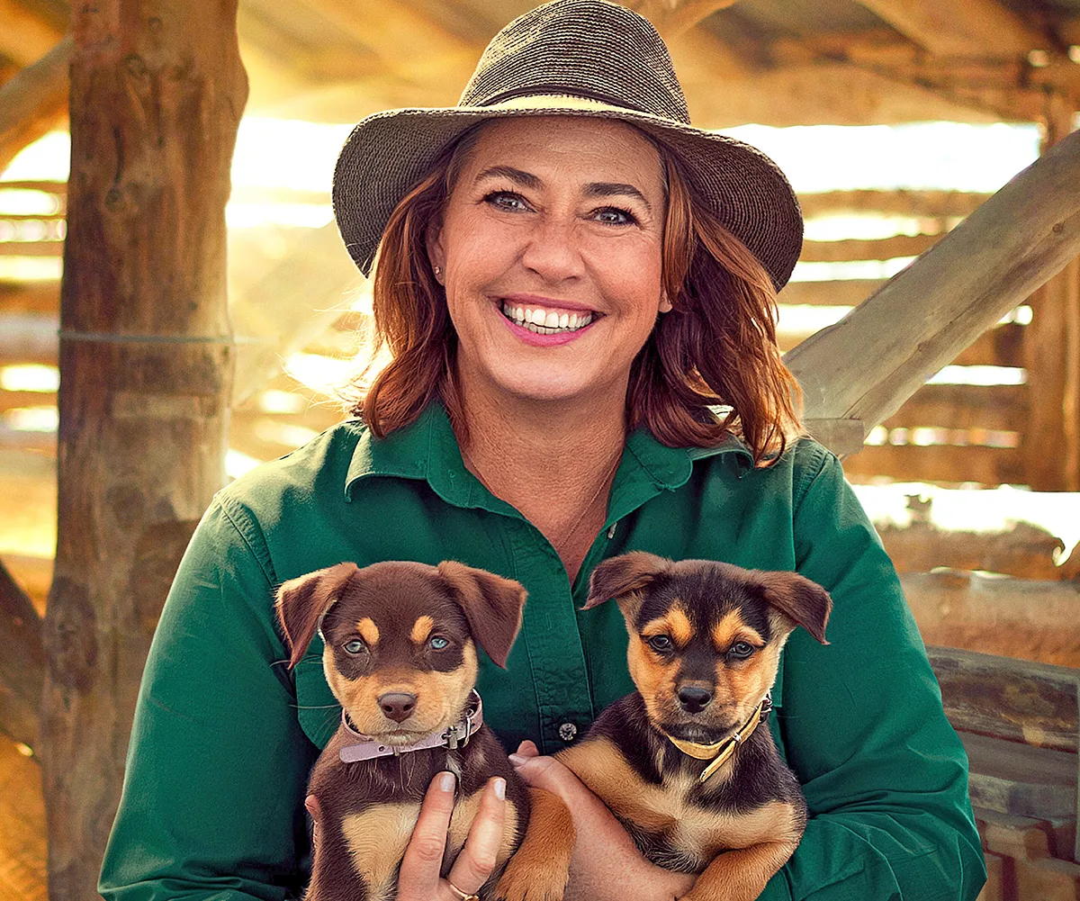 Lisa Millar, with a hat on, holds two puppies