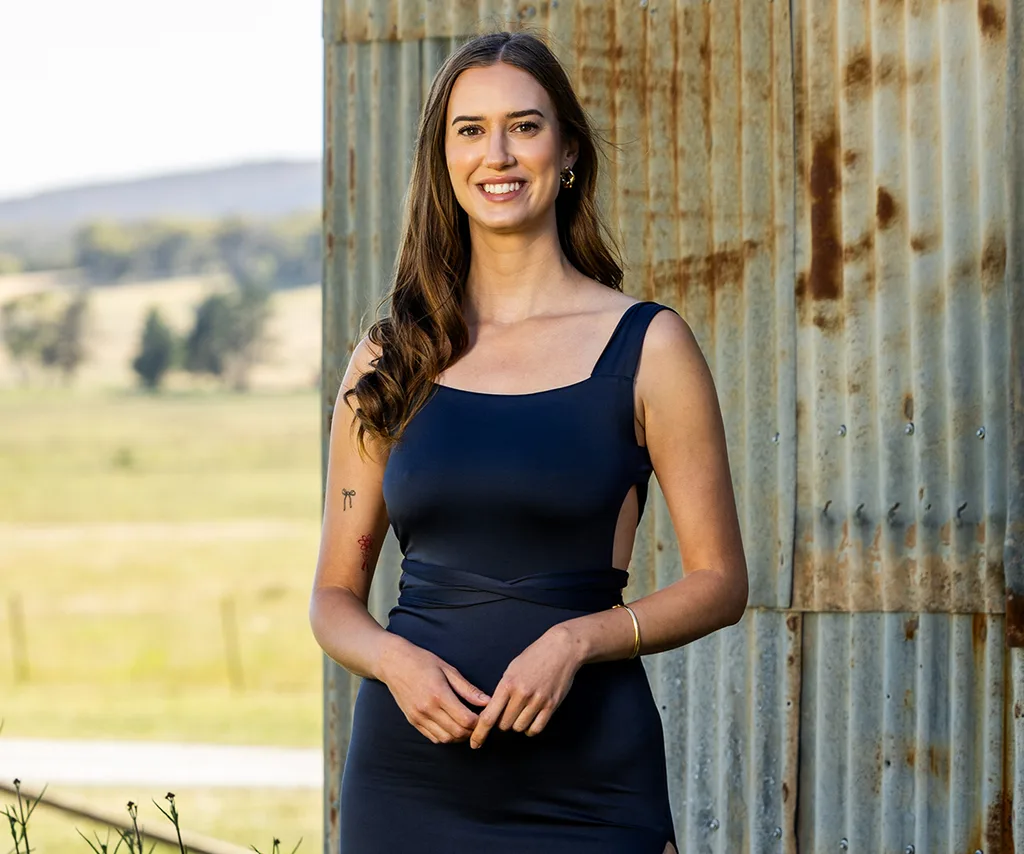 Yvonne, in a black dress, stands in front of a farm shed