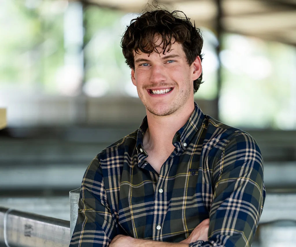 Zac, wearing a checked shirt, stands with his arms folded