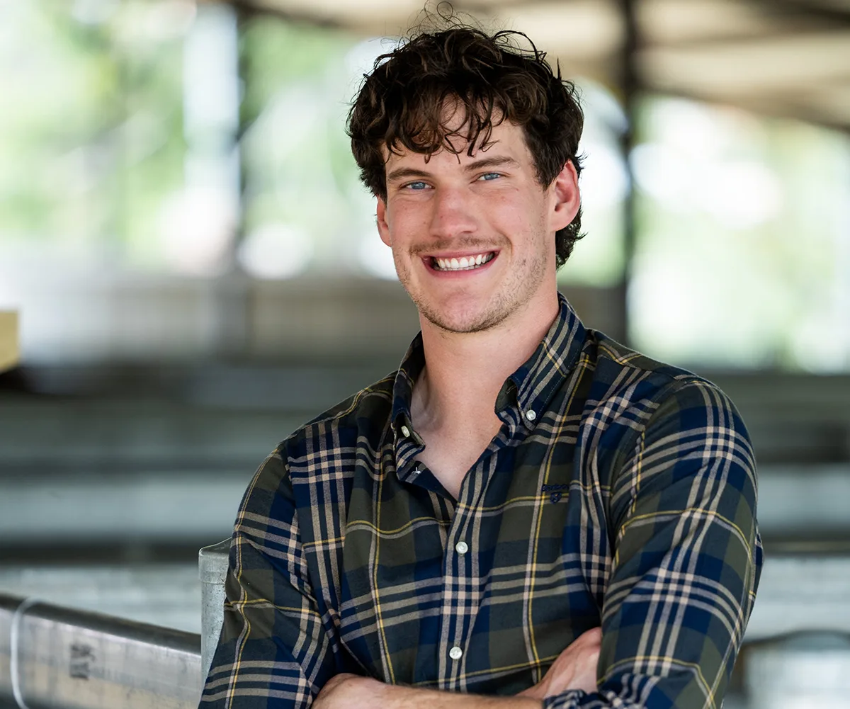 Zac, wearing a checked shirt, stands with his arms folded