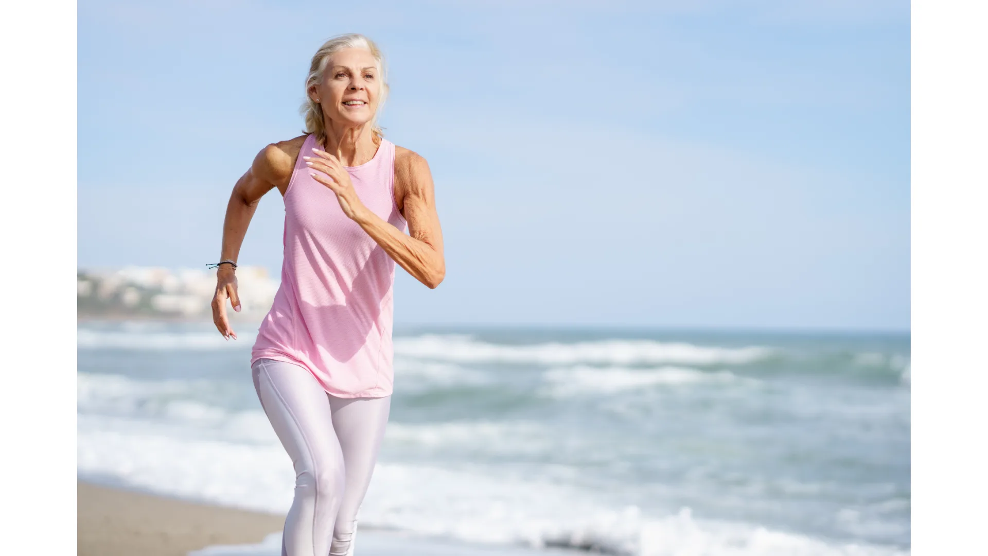 An older woman runs along a beach.
