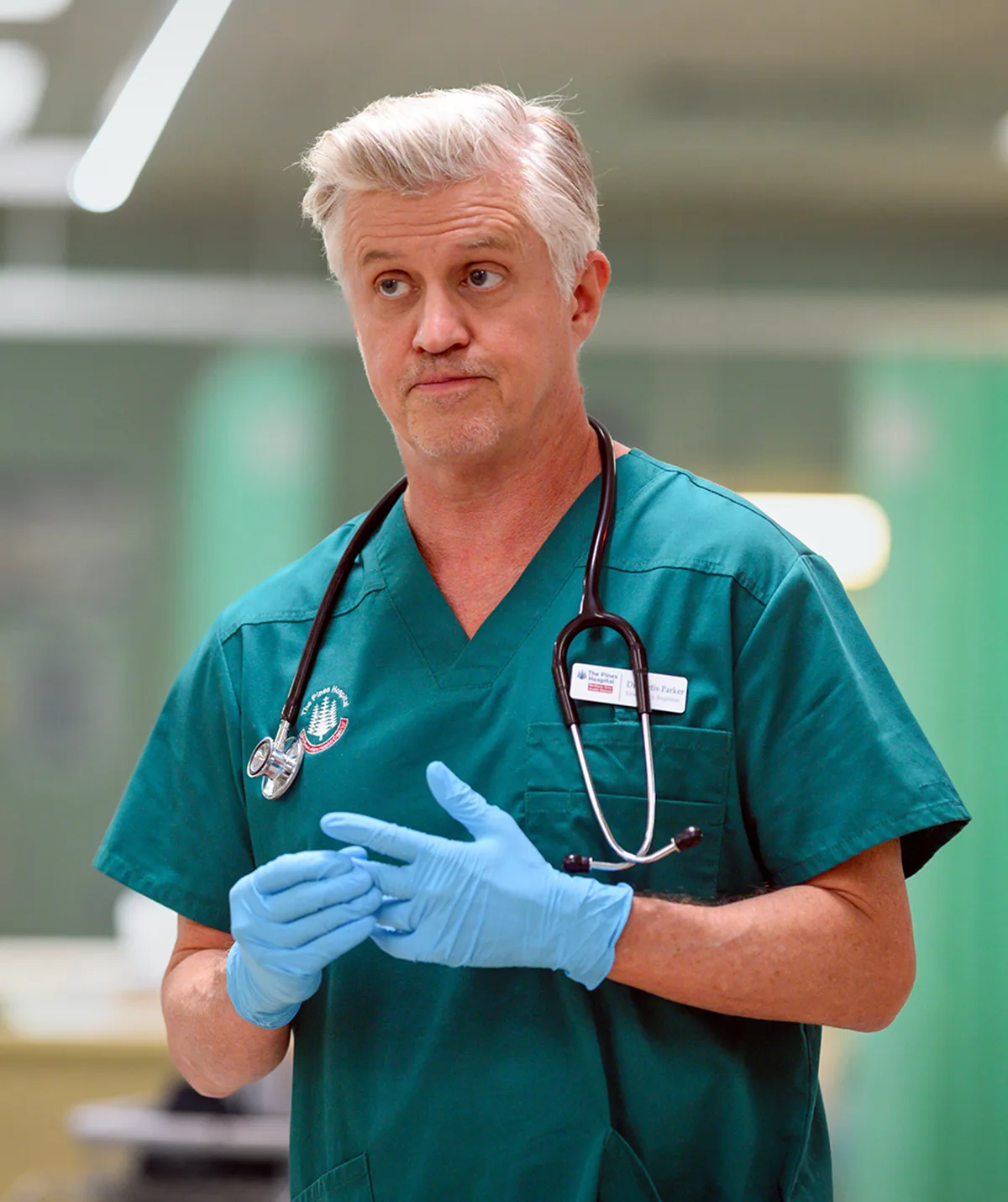 Dan Wyllie as Curtis in teal scrubs in a hospital on set of The F Ward.