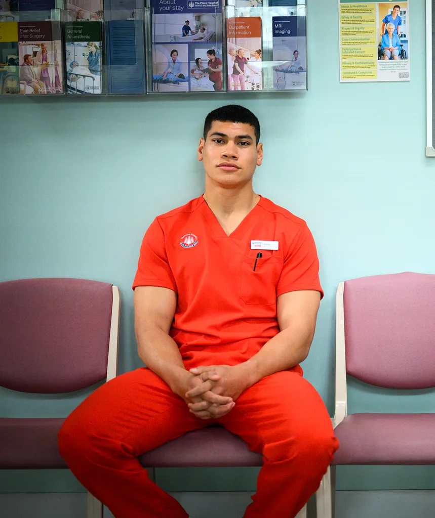 Ioane Sa'ula in red scrubs sitting in a hospital waiting room on set of The F Ward.