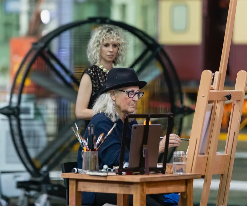 Judge Bree Pickering stands behind artist Cherie as she works on her painting