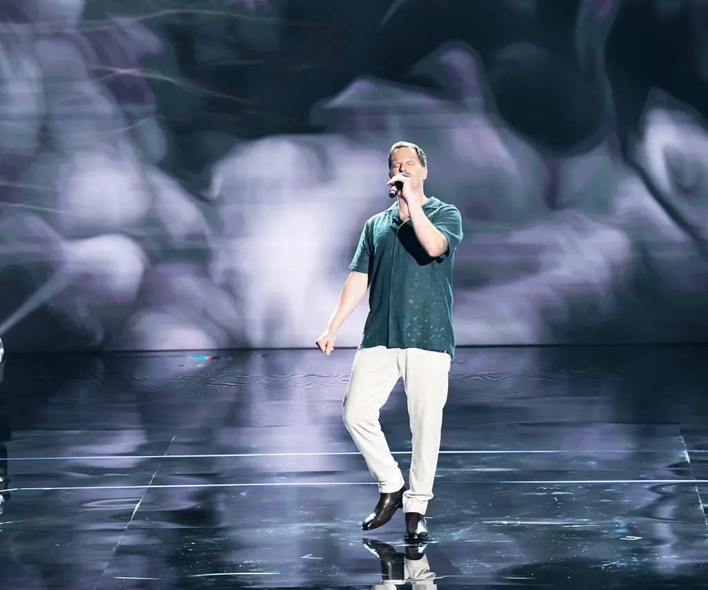 Jess, in a green shirt, sings on the stage of The Voice