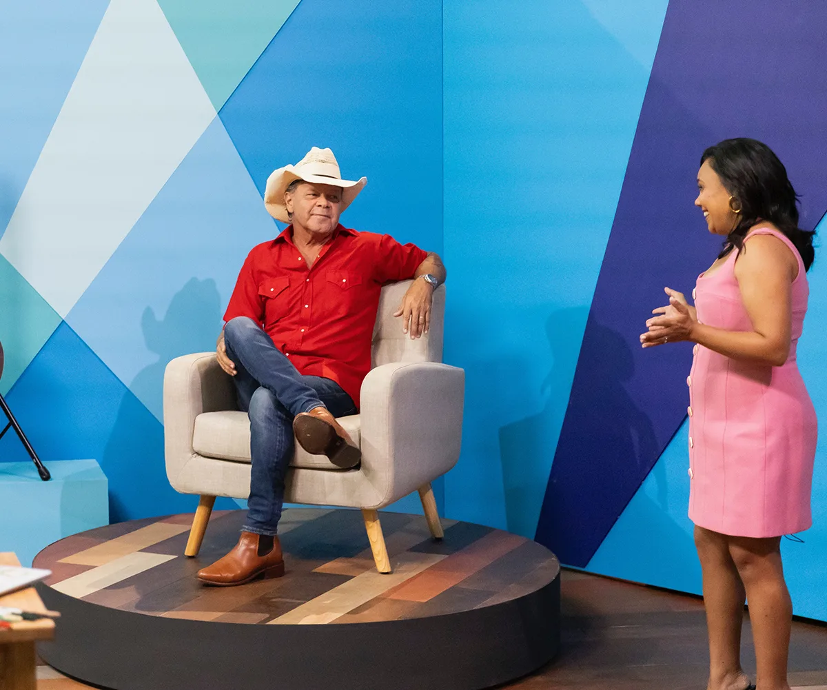 Miranda chats to Troy, sitting in a chair and wearing a cowboy hat