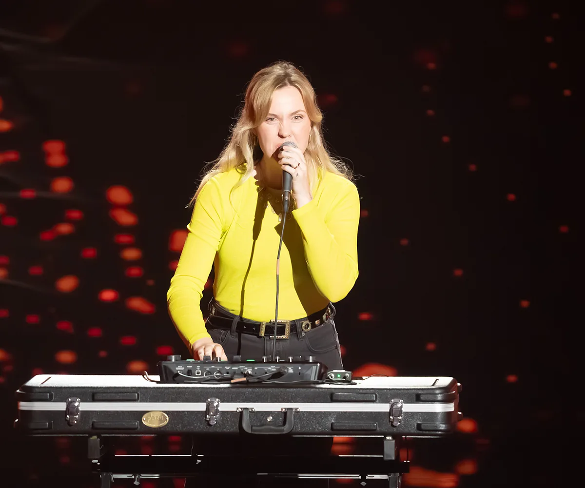 Edde sings into a microphone on the set of The Voice