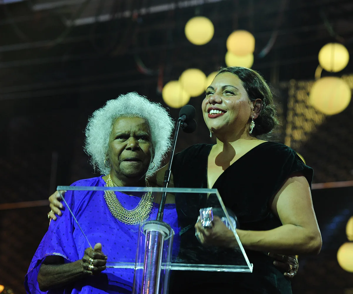 Deb standing on stage, with her arm around Bonita Mabo, at the 2013 Logie Awards 