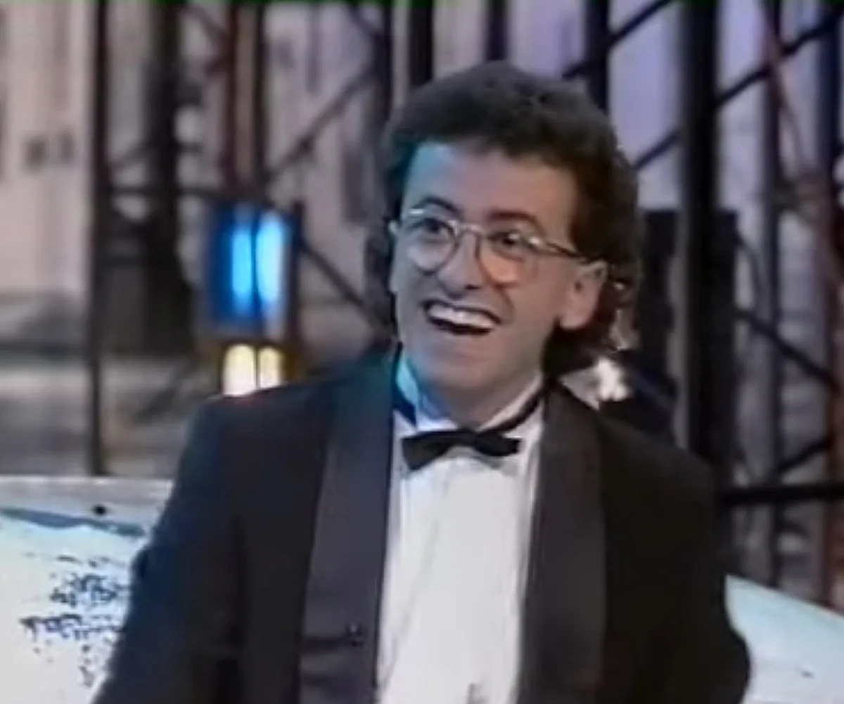 A young Andrew Denton, wearing a suite and a bow tie, on the set of The Money Or The Gun