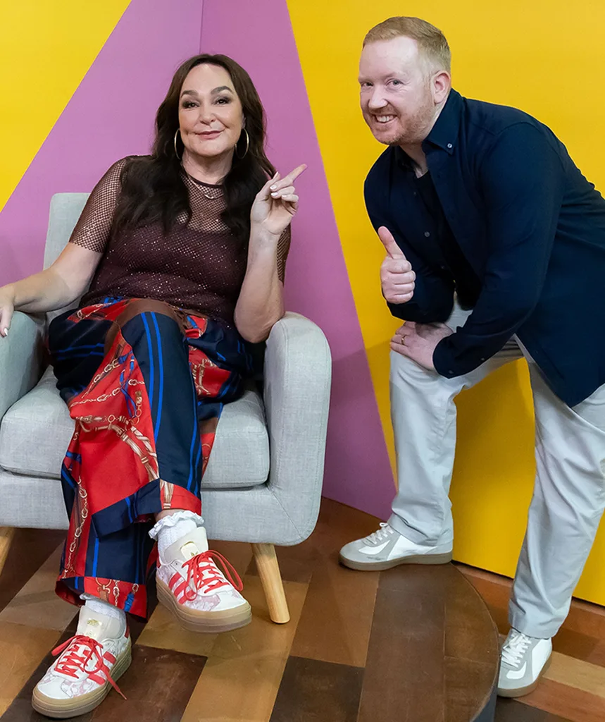 Kate sits in a chair while Luke stands close by on the set of Portrait Artist Of The Year
