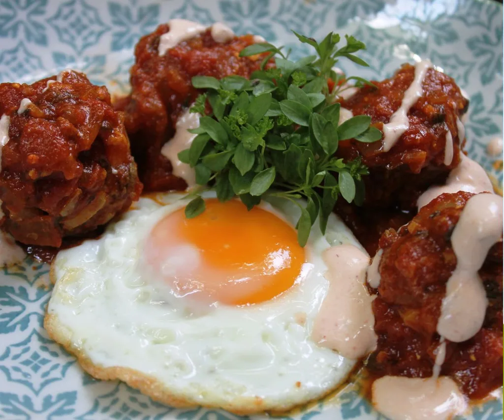 An egg and meat dish on a blue plate with a herb garnish.