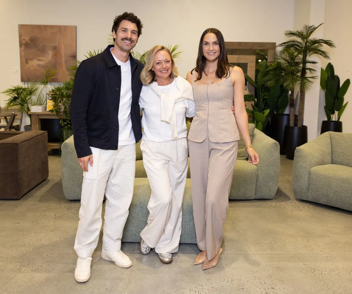 Matty J, Shelley Craft and Laura Byrne pose in front of green lounges while smiling.