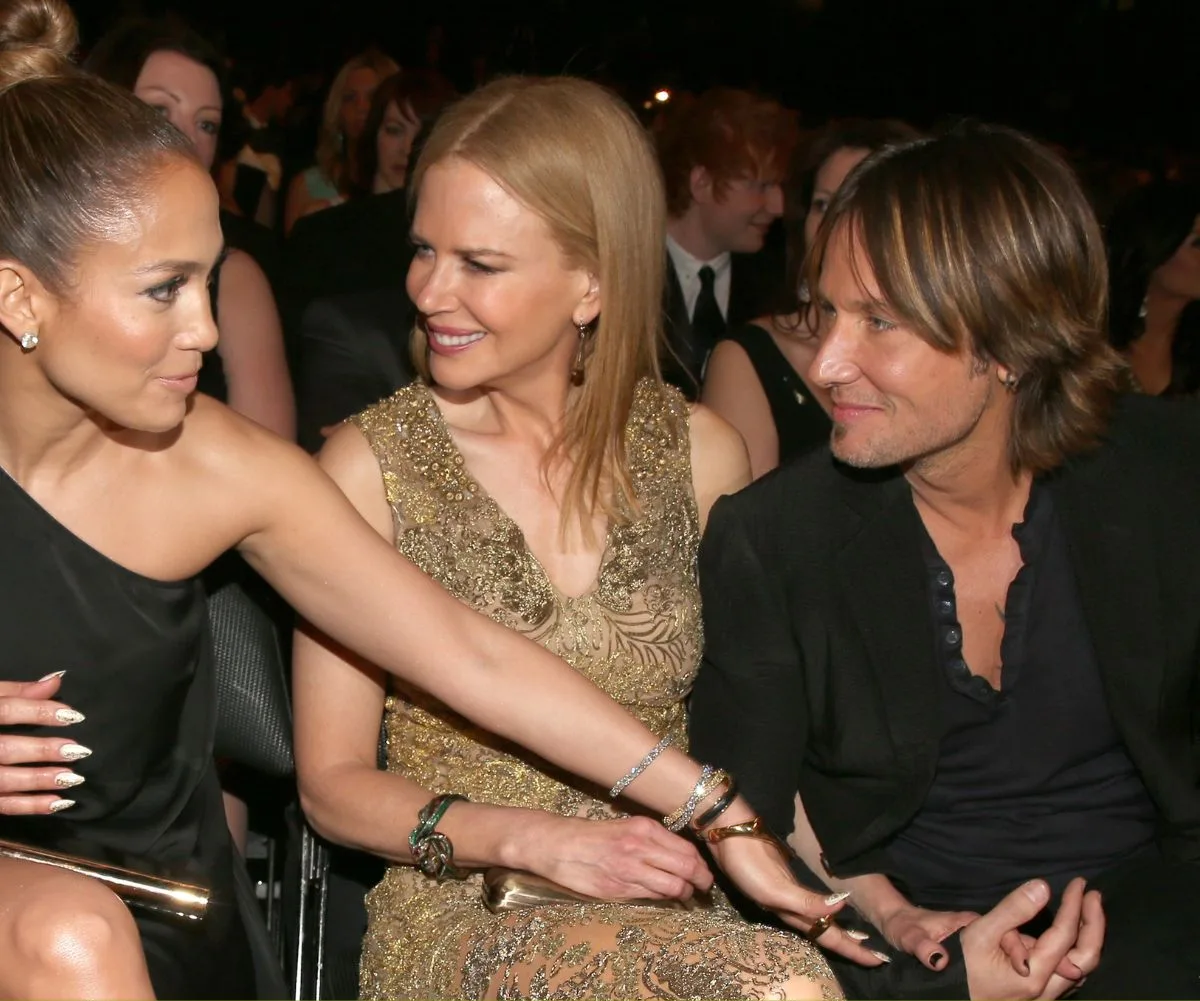 JLo reaches across to grab Keith's hand, with Keith's ex Nicole Kidman in between, all are smiling.
