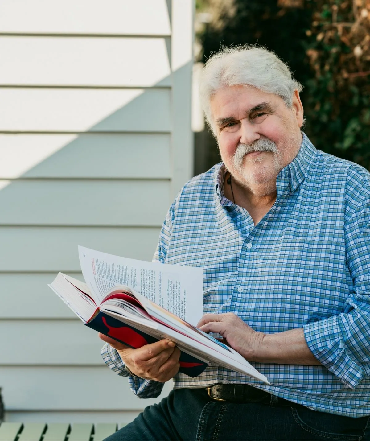 Huey wearing a blue shirt, smiling and holding his memoir. 