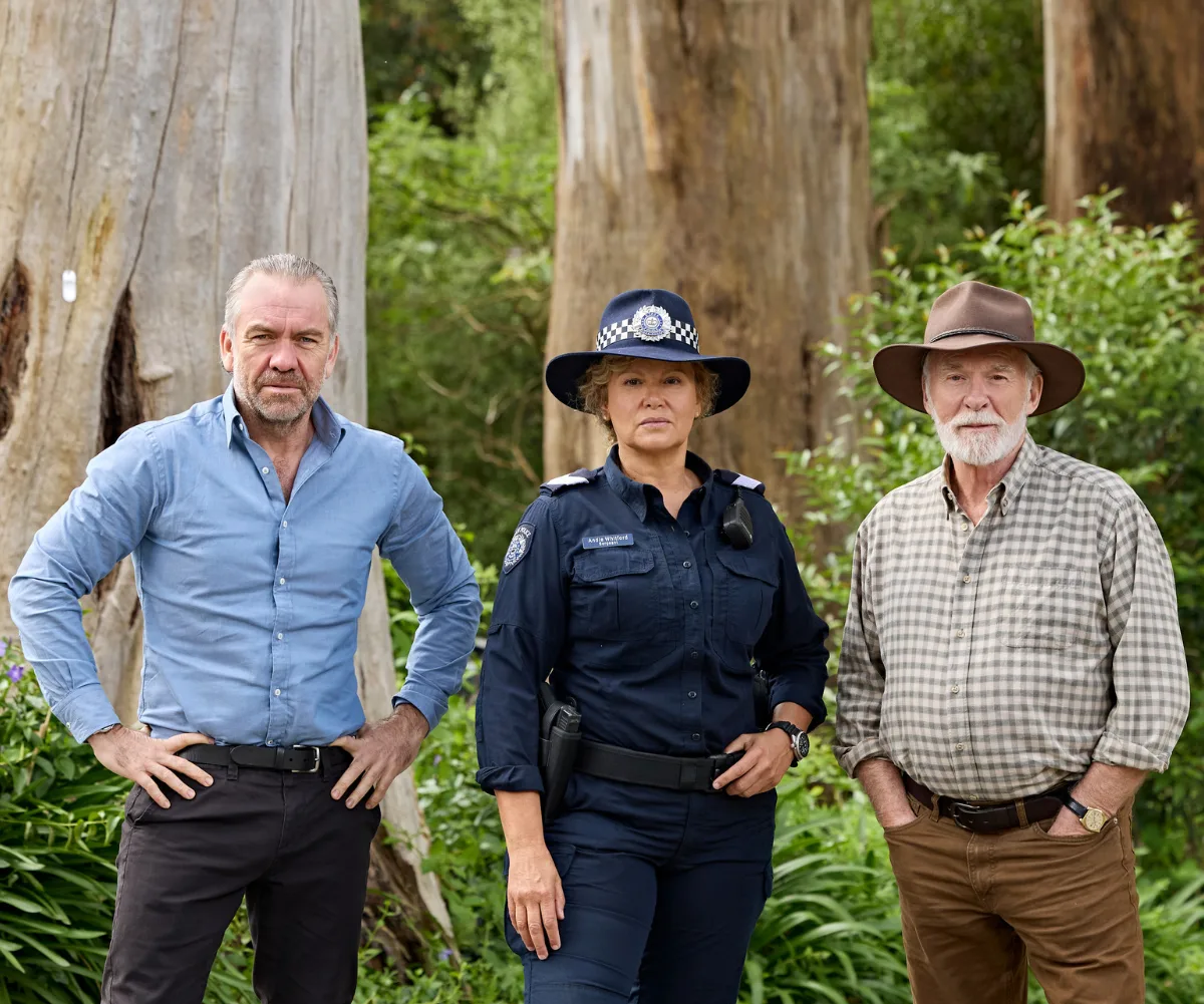 Leah stands in front of some trees with two other actors