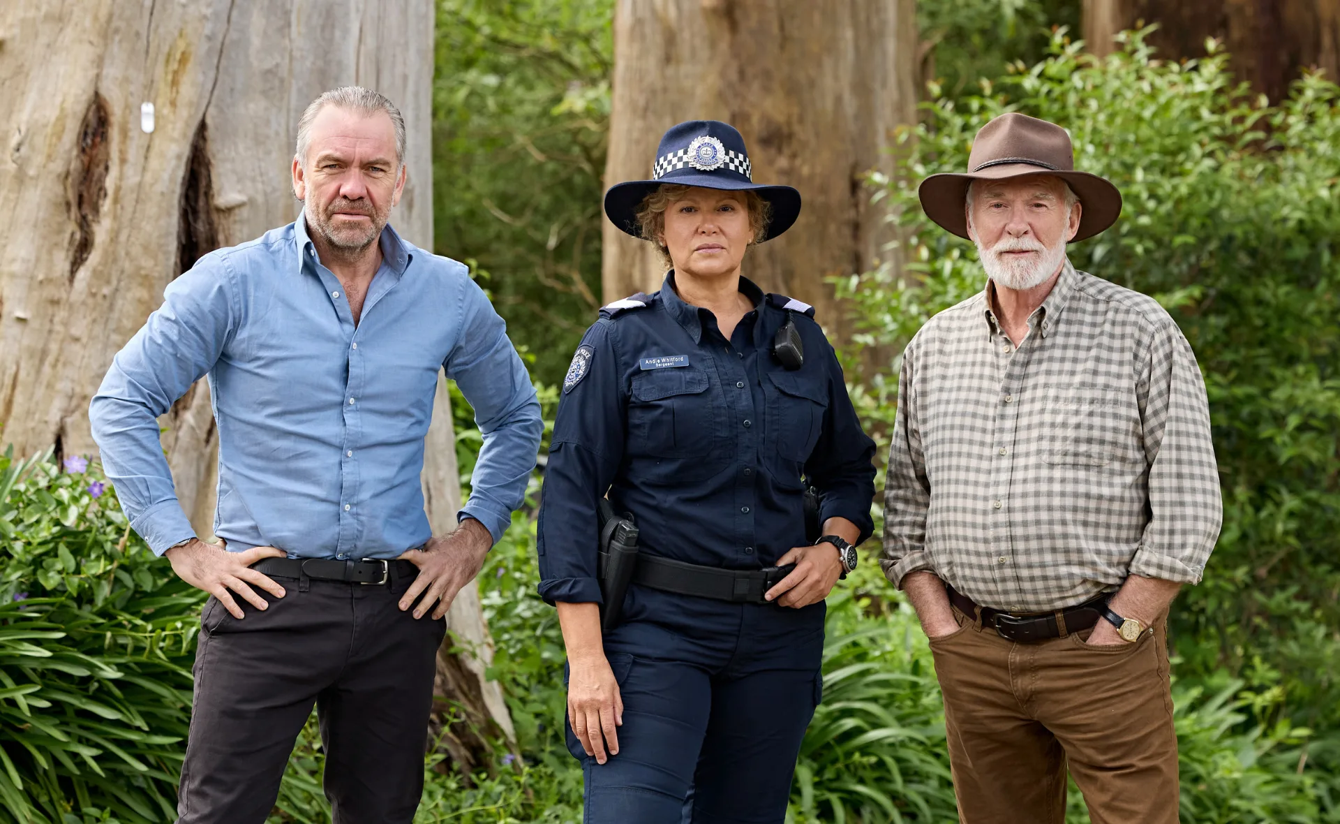 Leah Purcell, in police uniform, stands in front of trees with her co-stars