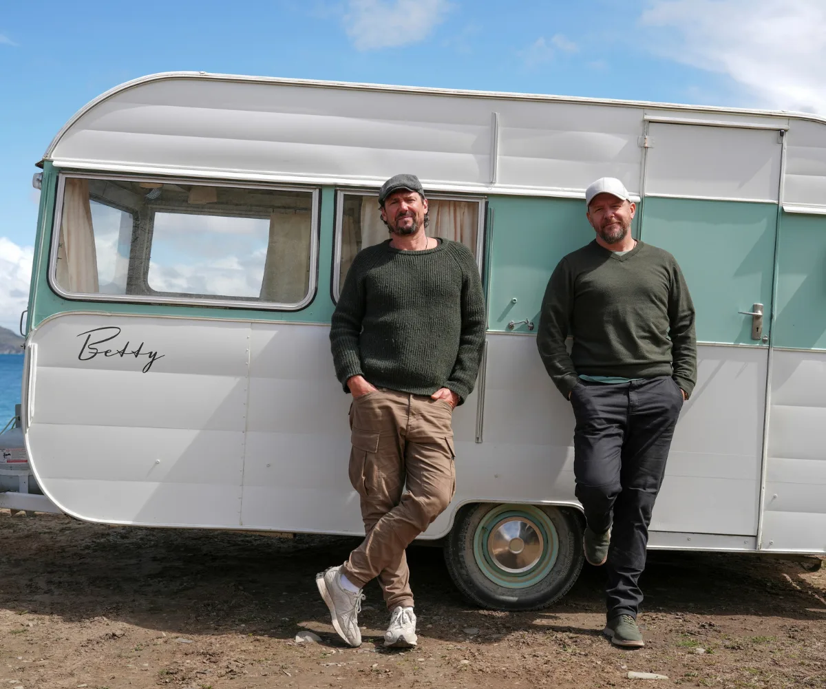Colin and Manu stand in front of a caravan in New Zealand