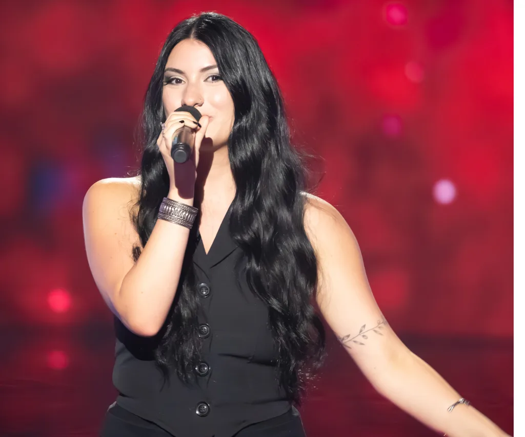 Victoria, wearing black, in front of a red background on The Voice