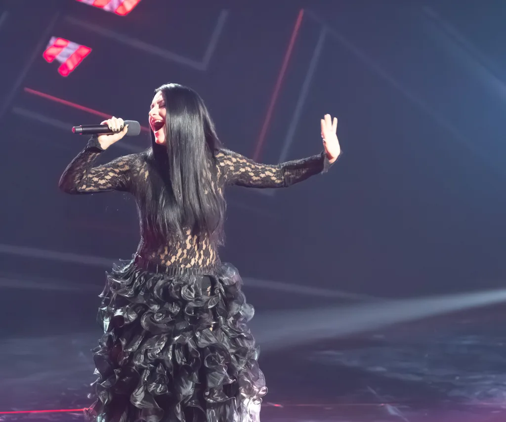 Victoria, in a long black dress, sings on the set of The Voice