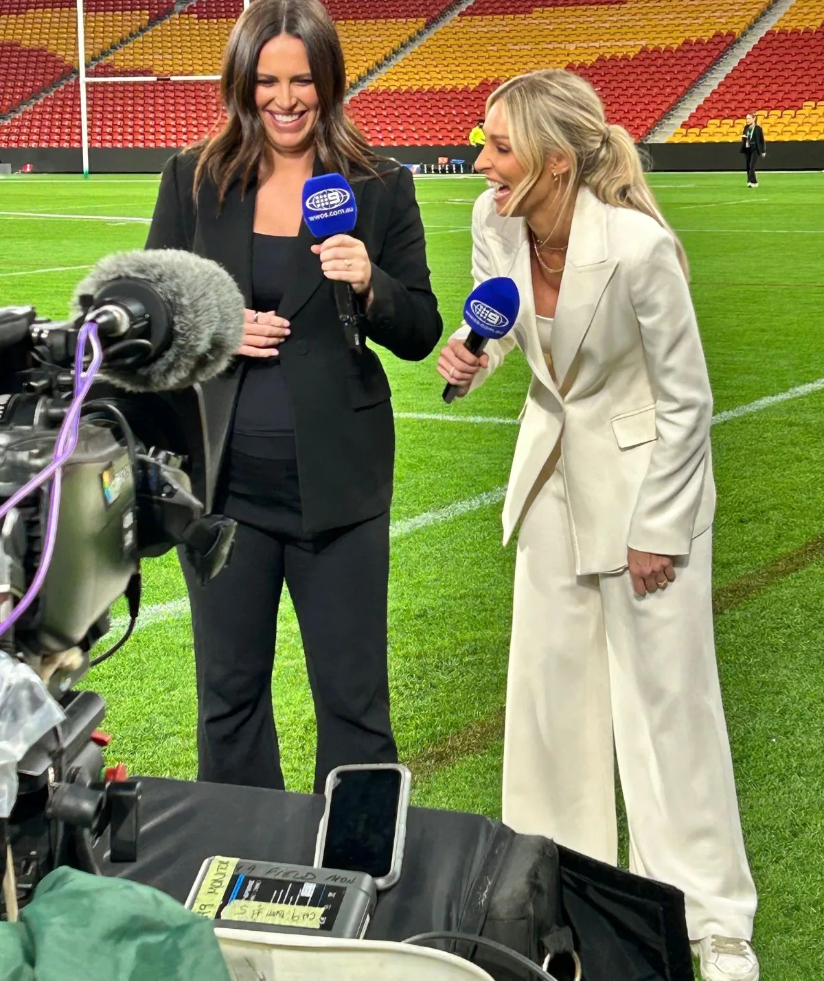 Danika Mason holds her pregnant stomach on a football field with a Channel Nine microphone