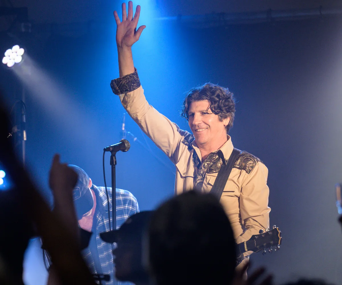 Peter Fenton, as Andy, stands on the stage with one arm up in the air