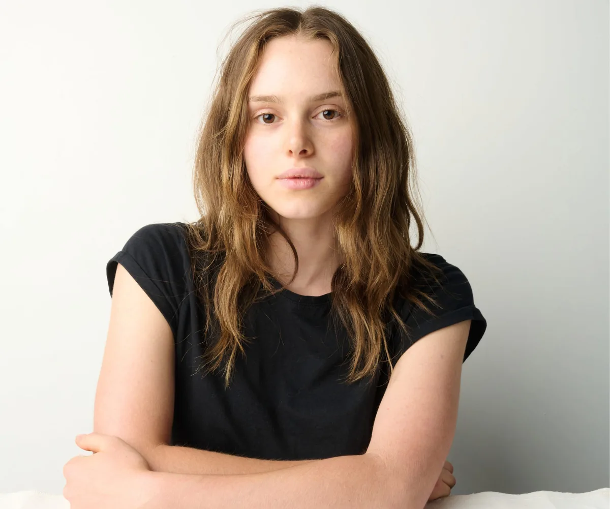 Zoe, wearing a black t-shirt, sits in front of a white background