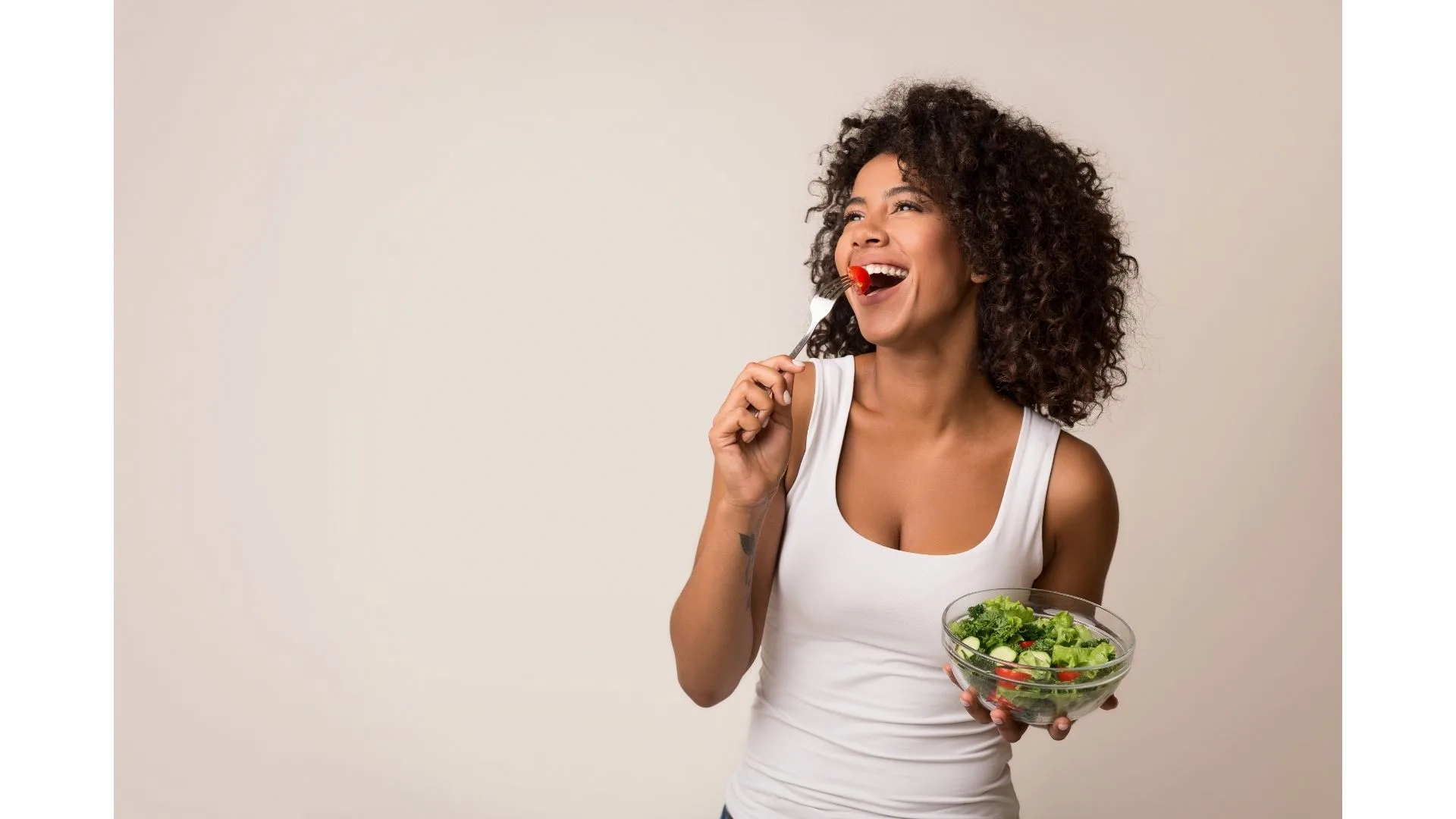 A woman happily eats a bowl of vegies.
