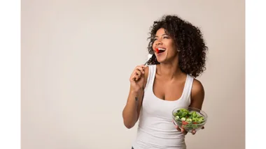 A woman happily eats a bowl of vegies.