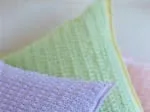 Crocheted cushions in pastel purple, green, and pink with a textured pattern.
