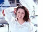 "Smiling woman in a white crochet top poses in front of boats."