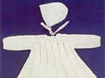 White christening gown and bonnet set on a dark background, part of the "Prince of Wales Feathers" collection.