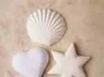 White bath bombs shaped like a heart, star, and shell on a beige surface.