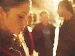 A young woman in focus looks down, with blurred people and a warm, glowing background.