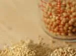 A measuring cup filled with grains sits behind a pile of dry oats on a wooden surface.