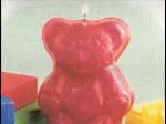Red teddy bear-shaped candle on a light surface with colorful blocks in the background.