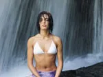 A person in a white bikini meditates in front of a waterfall.