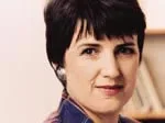 Laurie Graham, wearing a plaid shirt, looking towards the camera with bookshelves in the background.