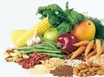 A variety of fresh fruits and vegetables, including corn, apples, carrots, and leafy greens, displayed on a white surface.