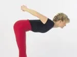 Woman in red leggings and black top performing a forward bend stretch with hands clasped behind her back.
