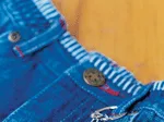 Blue denim fabric with button detail and attached beaded key ring on wooden background.