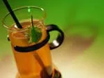 Tea in a glass mug with lemon and a straw against a green background.