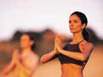 Two people practicing yoga outdoors at sunset, with the focus on a woman in a meditative pose.
