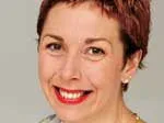 A woman with short hair and red lipstick smiles at the camera against a plain background.