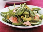 Plate of fresh spinach salad with avocado, salmon, and shrimp on a red tablecloth.