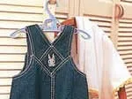 Denim cross-stitch overalls with embroidered rabbit on a hanger, beside a white towel on a wooden rack.