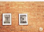 Two framed black and white photographs on a brick wall.